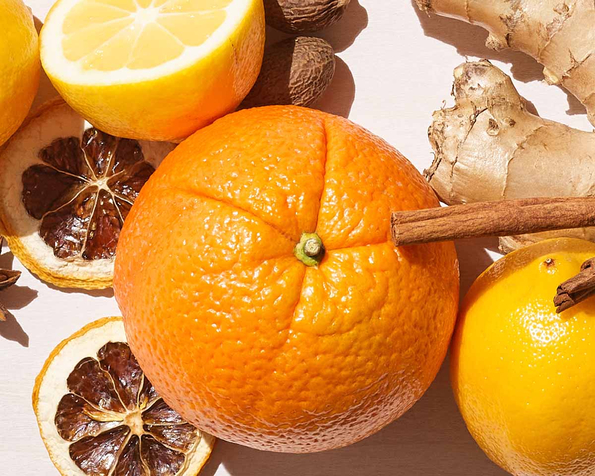 Orange with cinnamon stick surrounded by lemons, ginger, and dried citrus on a light background