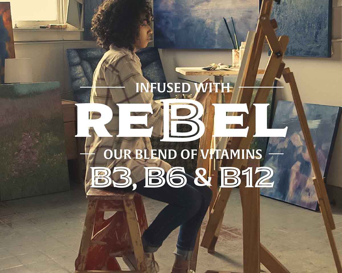 Person sitting on a stool in an art studio with paintings and text about vitamins B3, B6, and B12.