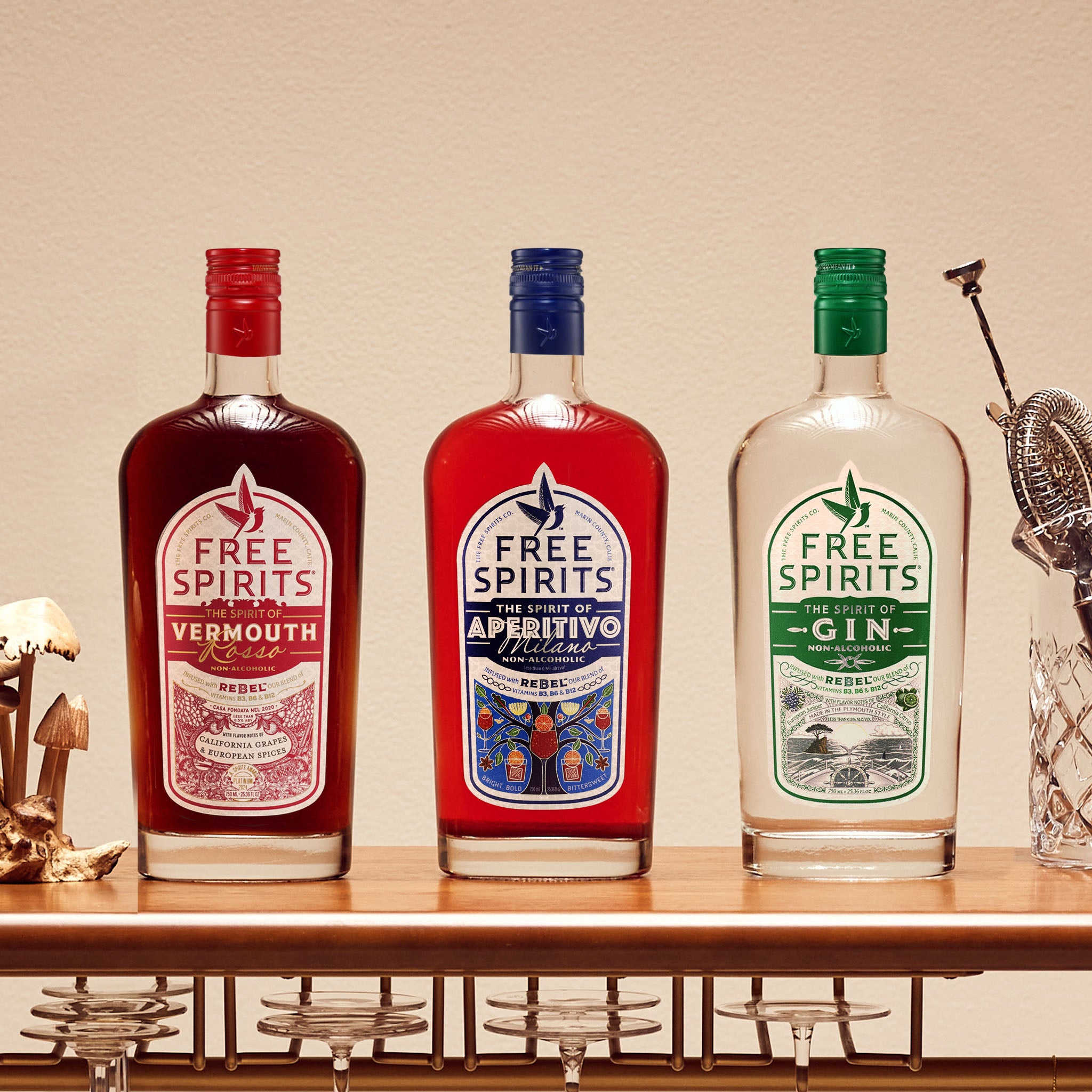 Three bottles of Free Spirits Vermouth, Aperitivo, and Gin on a bar shelf with decorative items.