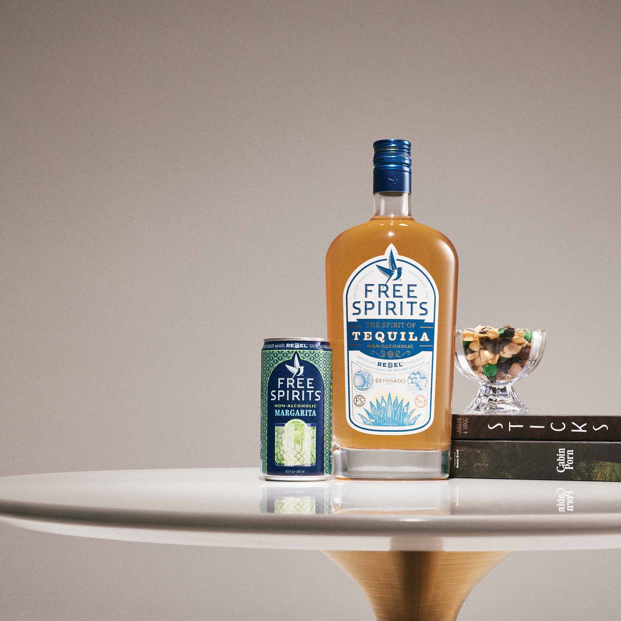 A bottle of Free Spirits Tequila and a matching can of Margaritas are styled on a white table against a neutral beige background