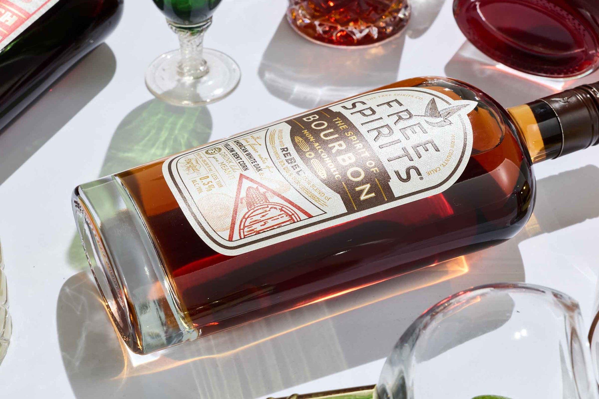 Bottle of Free Spirits Bourbon Alternative  on a reflective surface with glasses in the background