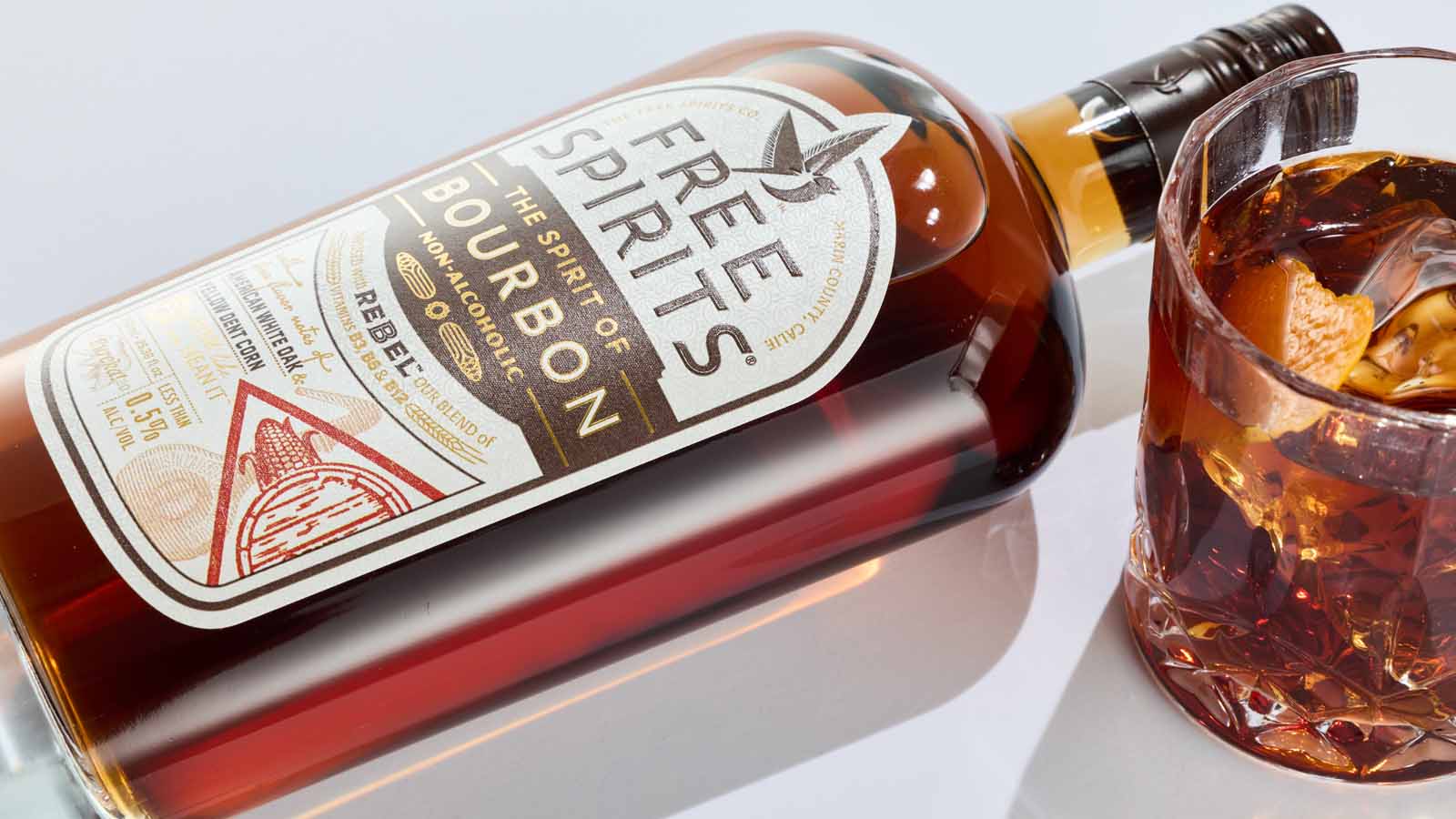 Bottle of Free Spirits Bourbon alternative with a glass of whiskey on a white background
