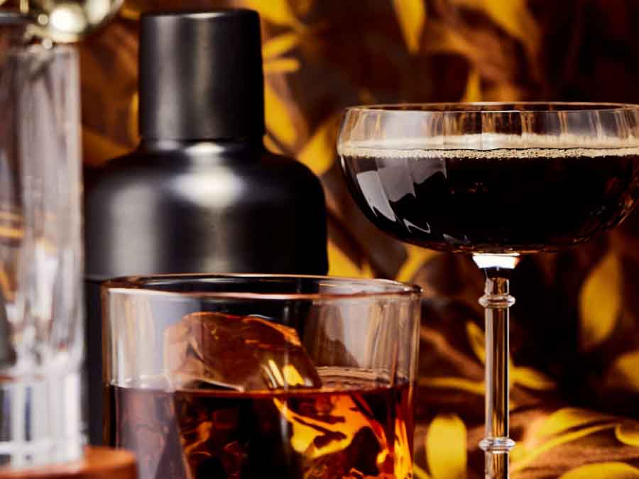 Two glasses with dark liquids, one with ice cubes, against a warm-toned background.
