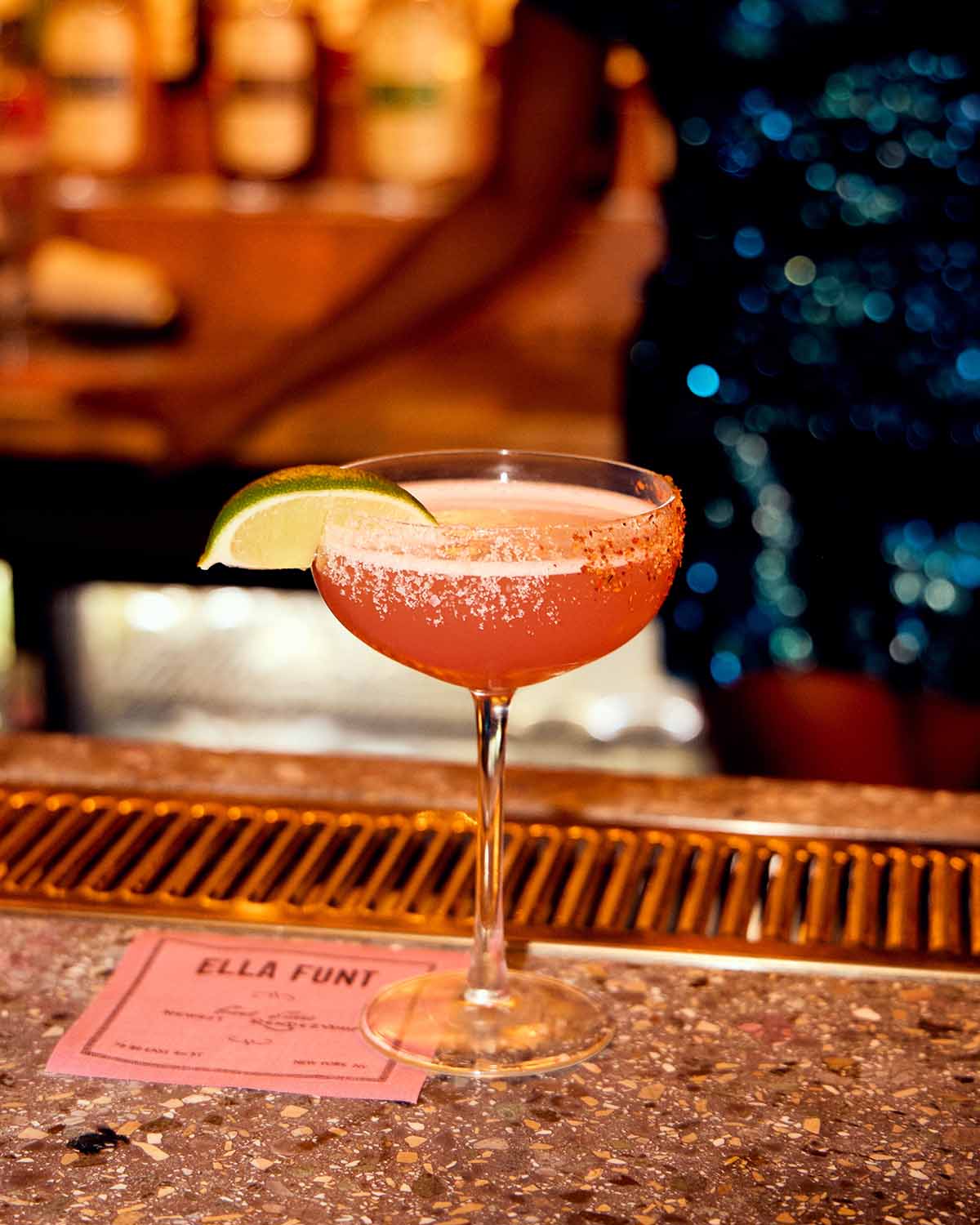Cocktail with a lime wedge on a bar counter with a blurred bar background