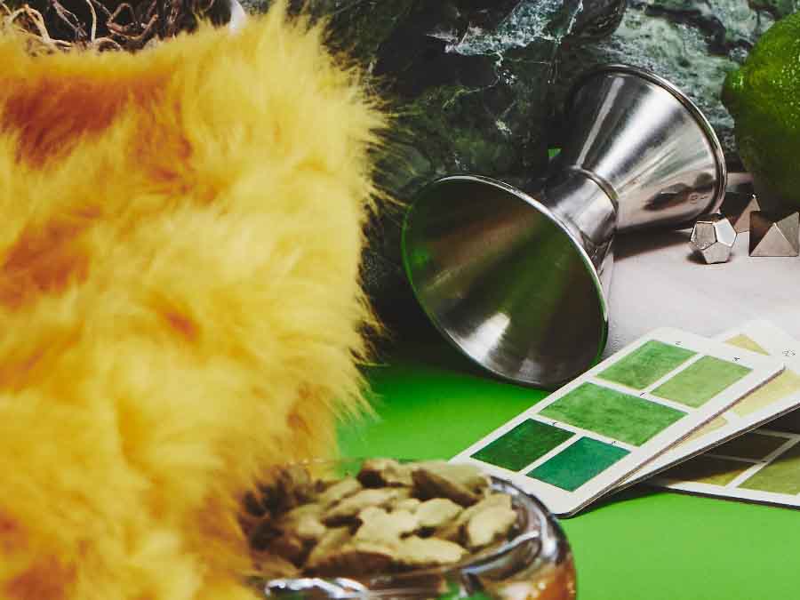 Close-up of a cocktail shaker, green color swatches, and a textured yellow object on a green surface.