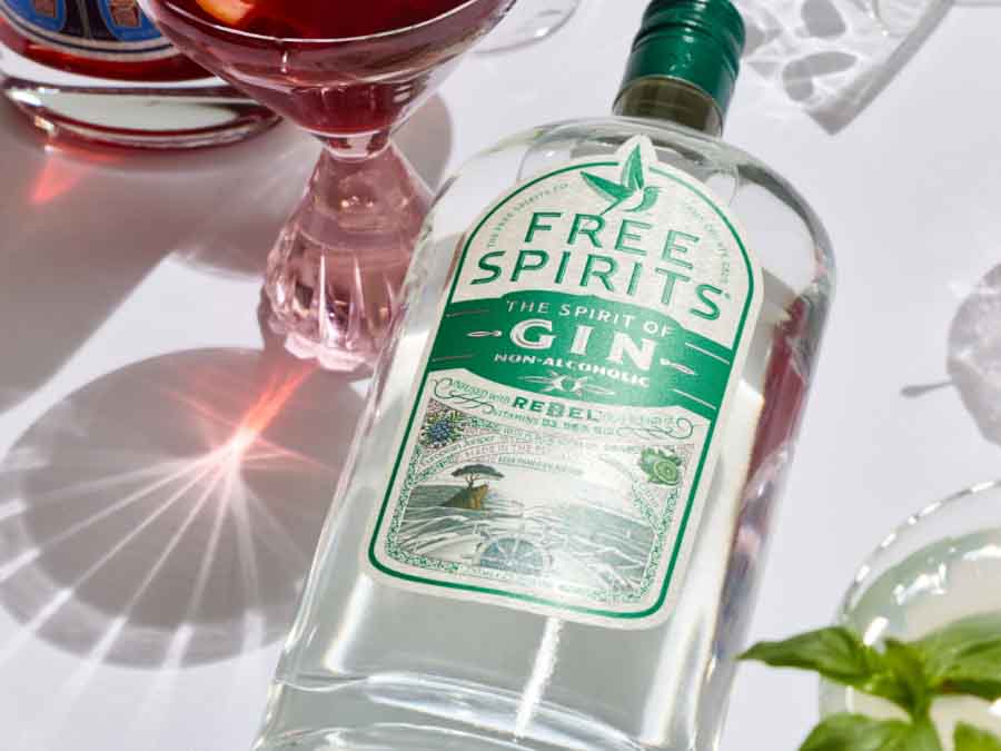 Bottle of Free Spirits gin alternative on a table with a red cocktail in the background
