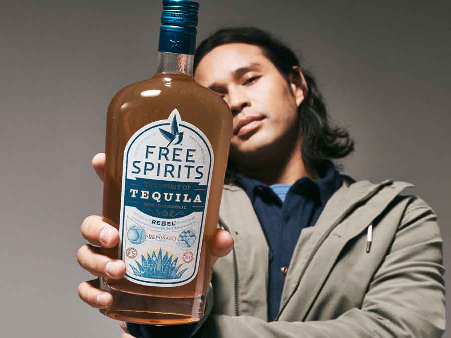 Person holding a bottle of Free Spirits Tequila against a gray background