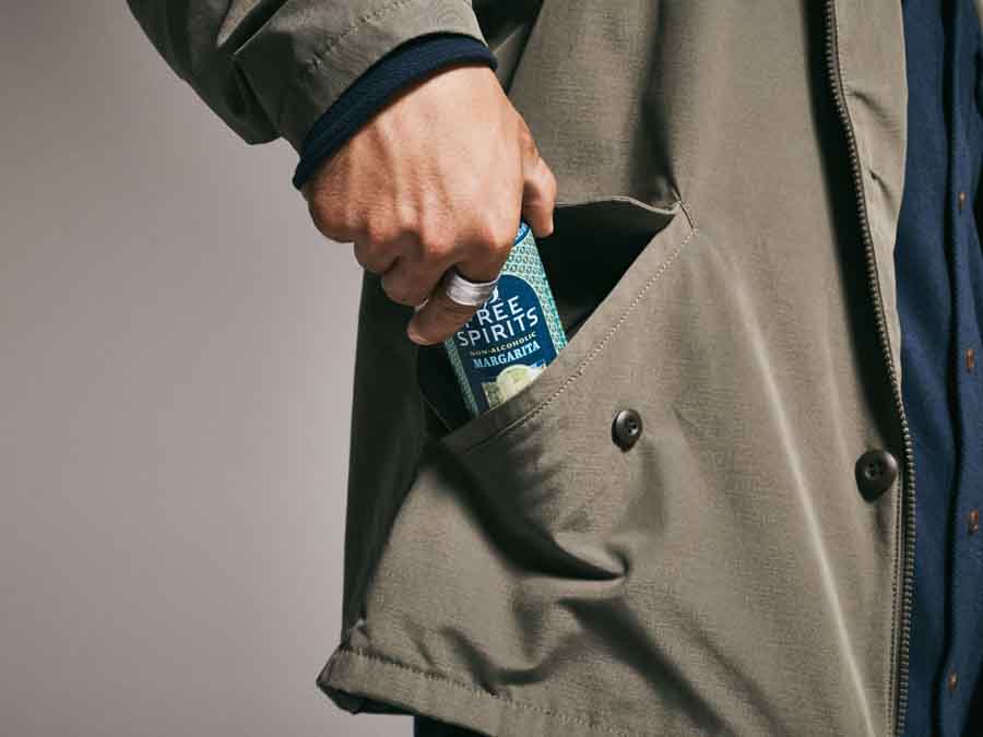 Person placing a can of Free Spirits margarita into a coat pocket against a neutral background