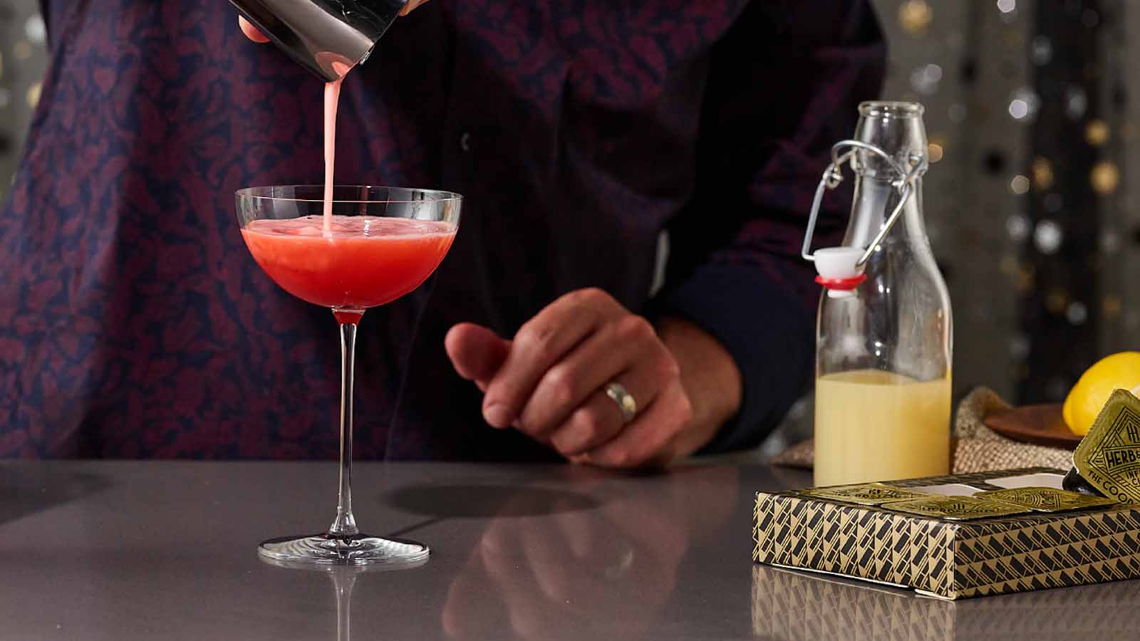 Person pouring a pink cocktail into a glass with a blurred background