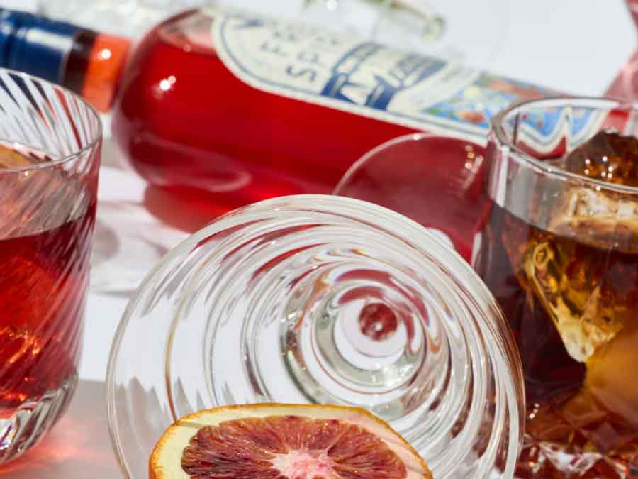 Close-up of a bottle and glasses with red aperitivo on a white surface