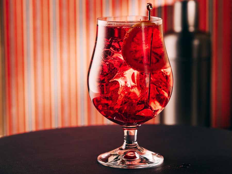 Red cocktail with ice and a cherry in a glass against a striped background