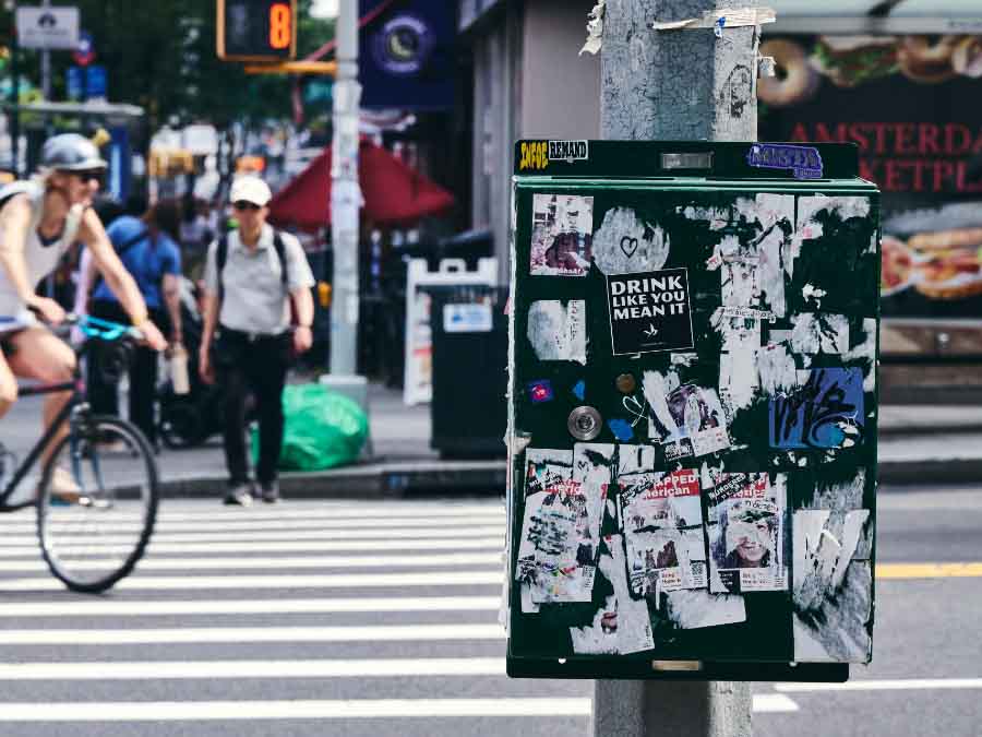 City street scene with a person on a bicycle, pedestrians, and a poster on a pole.