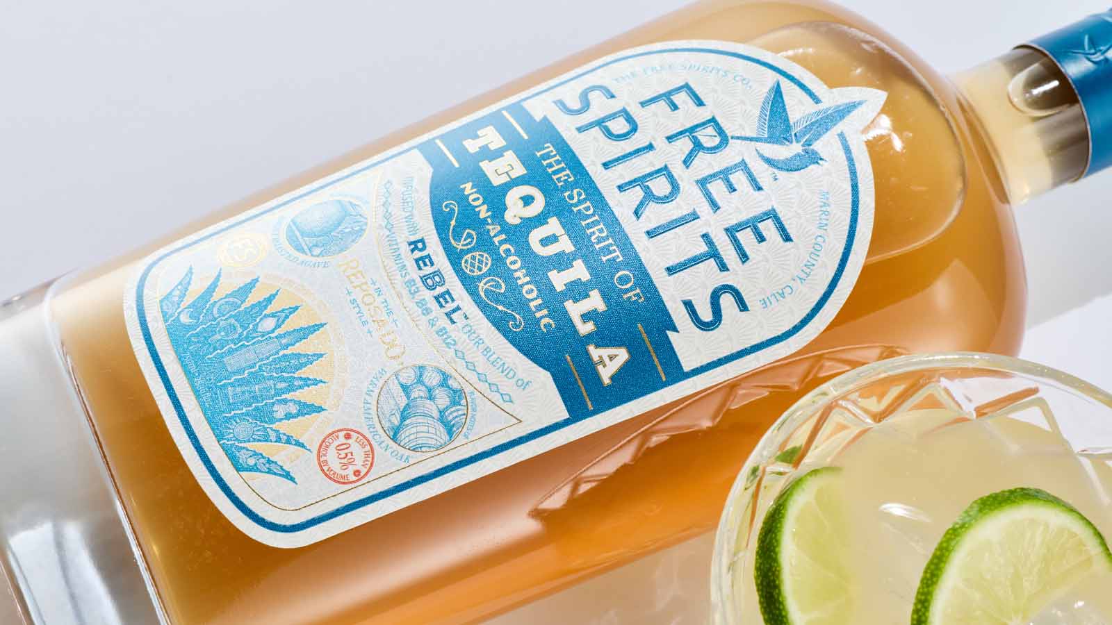 Bottle of Free Spirits tequila alternative with a cocktail garnished with lime slices on a white background