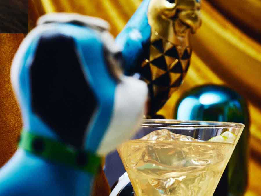 A maragarita with metal bird and vintage stuffed dog in a closeup shot with a gold background