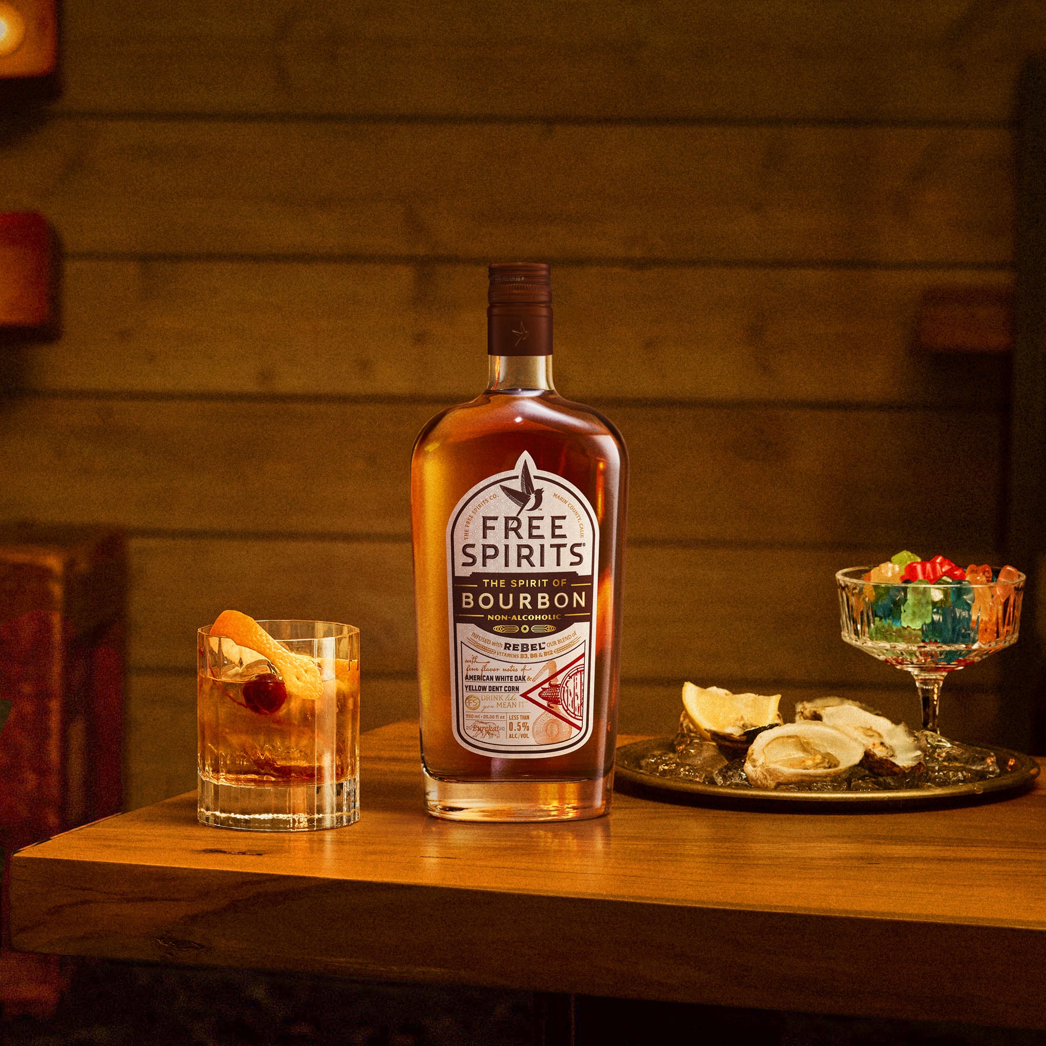 Bottle of Free Spirits Bourbon on a wooden surface with a glass and garnishes.