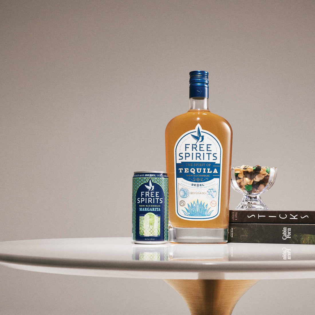A bottle of Free Spirits Tequila and a matching can of Margaritas are styled on a white table against a neutral beige background