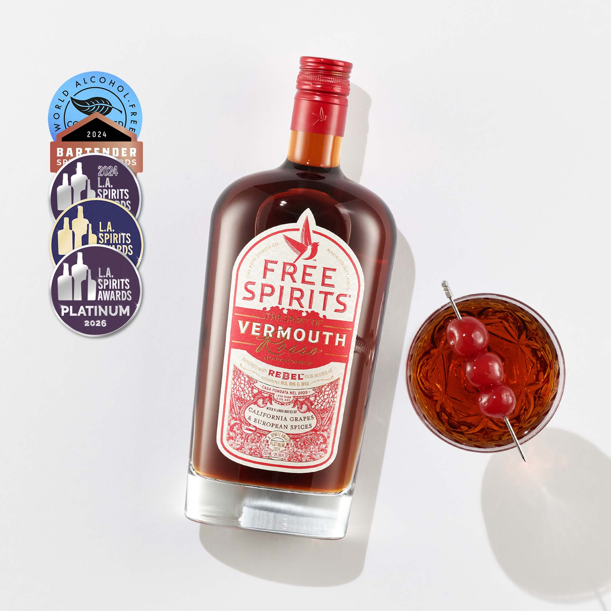 Bottle of Free Spirits Vermouth with a cocktail garnished with cherries on a white background