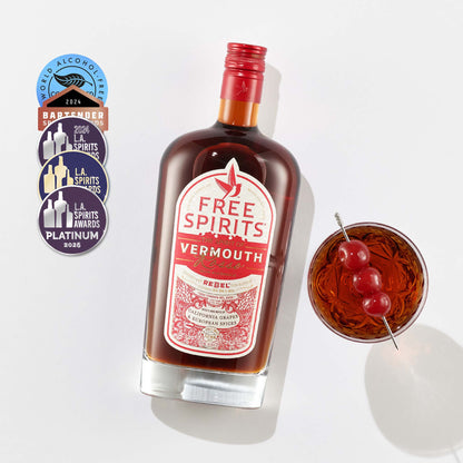 Bottle of Free Spirits Vermouth with a cocktail garnished with cherries on a white background