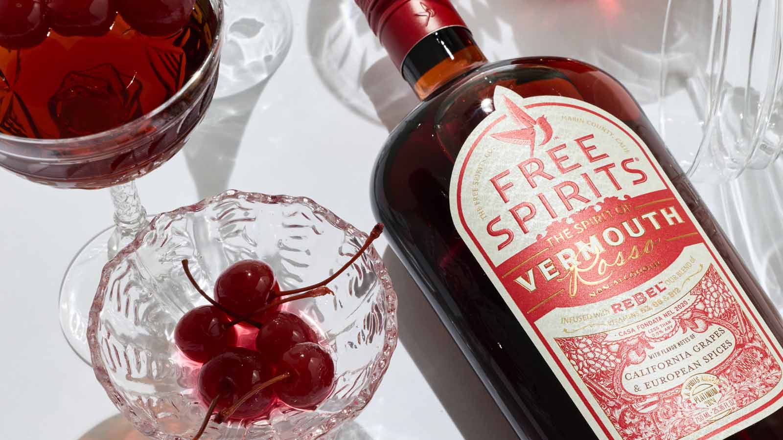 Bottle of Free Spirits vermouth with a cocktail and cherries on a white background