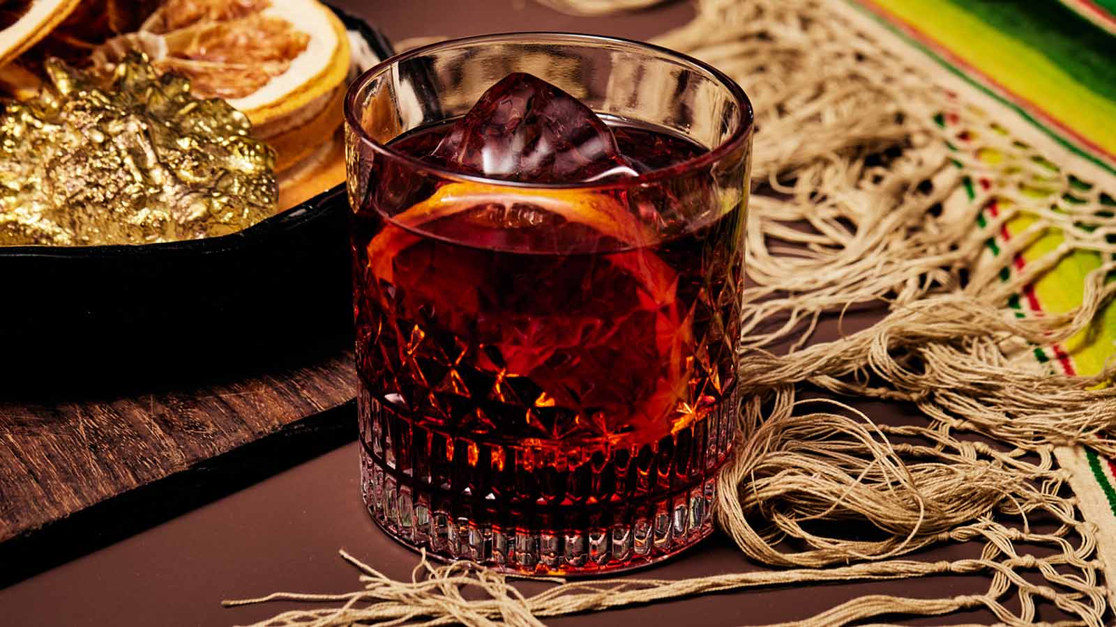 Vermouth based cocktail with ice and an orange slice on a textured surface