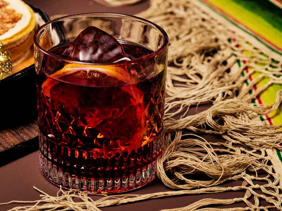 Dark cocktail with ice cubes on a textured surface