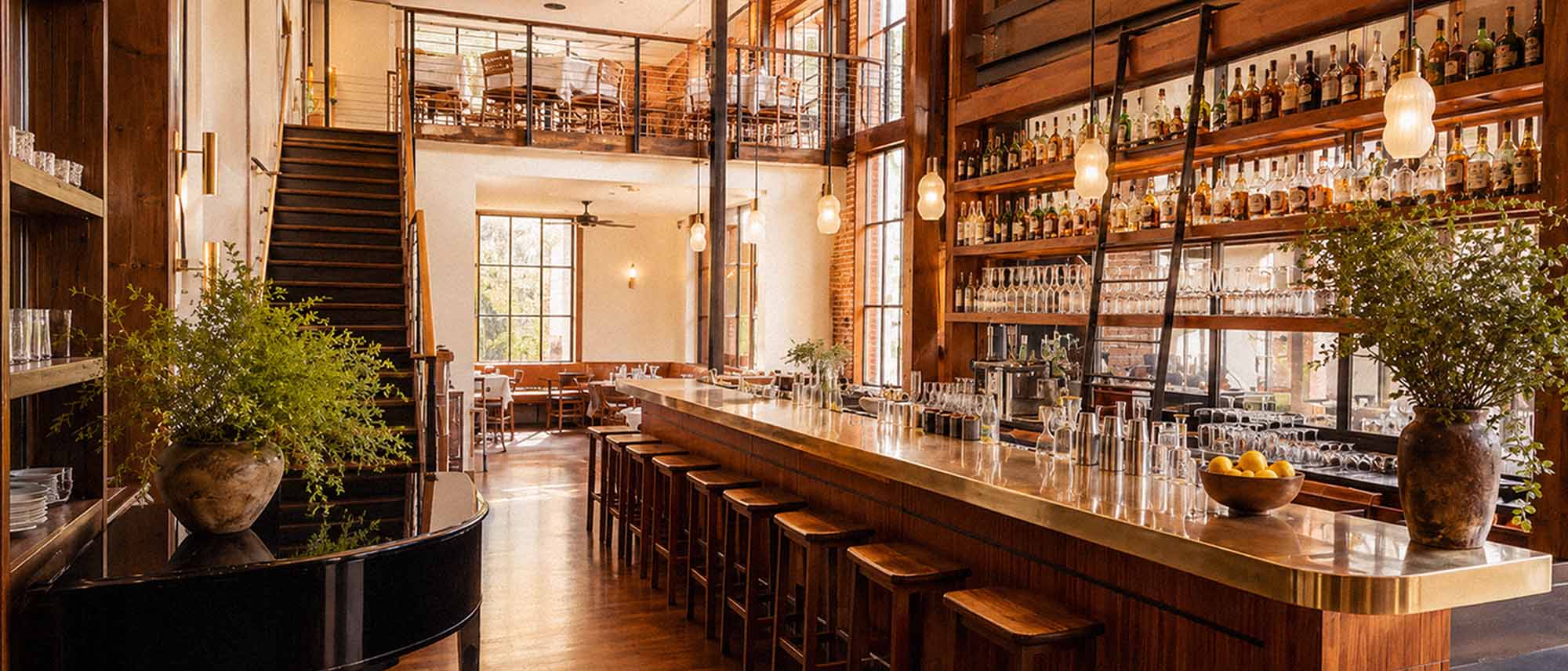 Modern bar interior with wooden counter, stools, and shelves filled with bottles.
