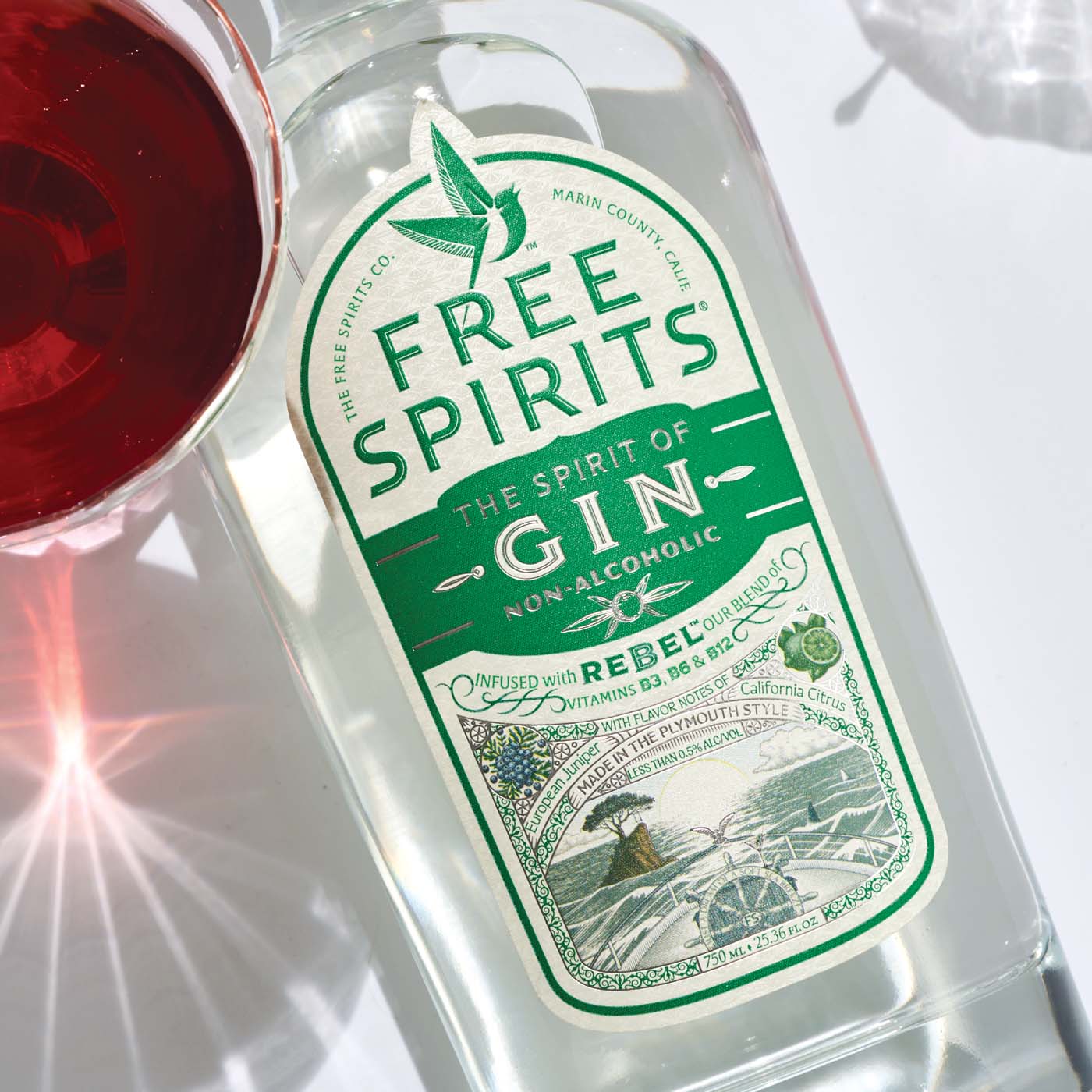 Bottle of Free Spirits non-alcoholic gin with a glass of red liquid on a white background